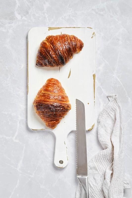 Top view of crispy croissant on white serving board on marble background