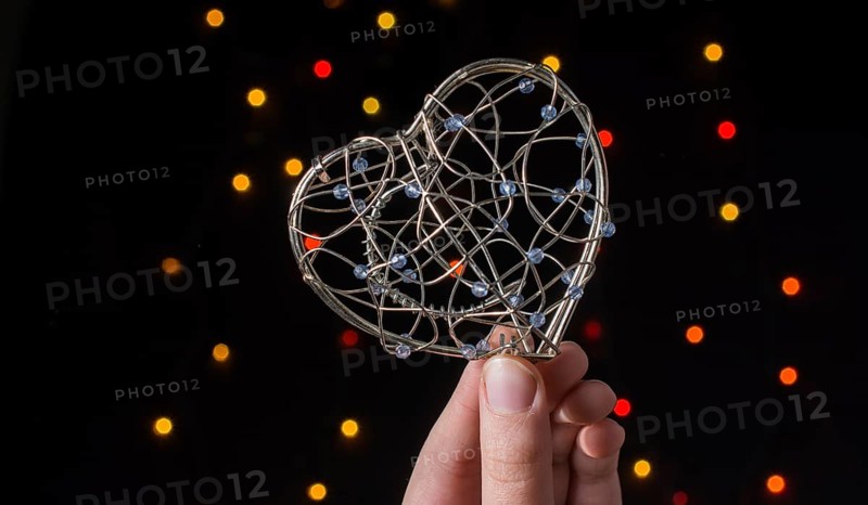 Heart shaped metal cage in hand on bokeh light background