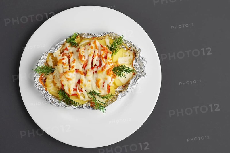 Top view of fried in foil sea fish and potato with paprika and cheese on gray background