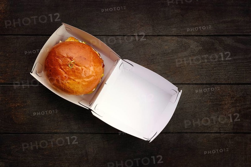 Top view of open take away box with burger on wooden table