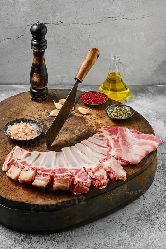 Raw lamb flap ribs with ingredients for cooking on wooden log