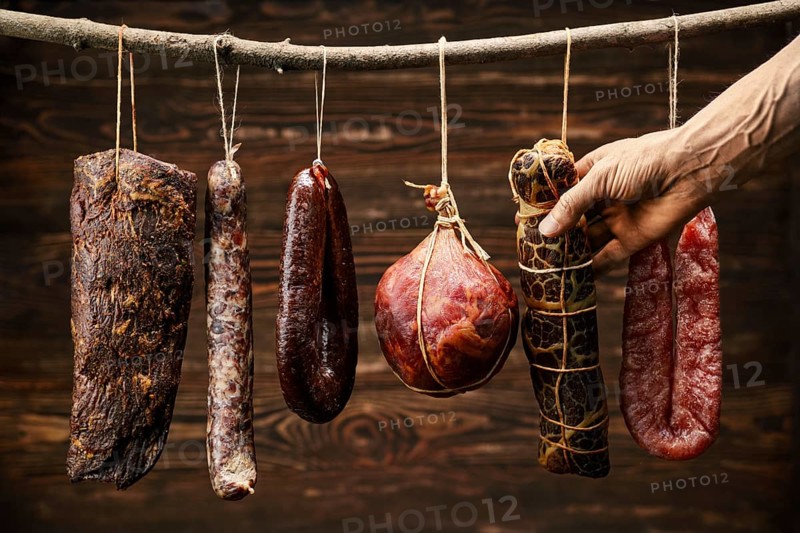 Assortment of dried meat and sausages hanging on a stick in a barn