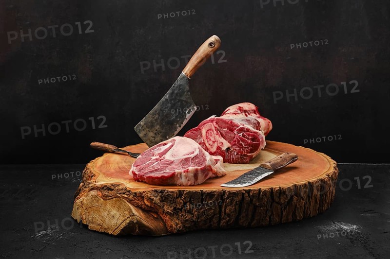 Chopping ossobuco steak from beef shank with cleaver on wooden stump