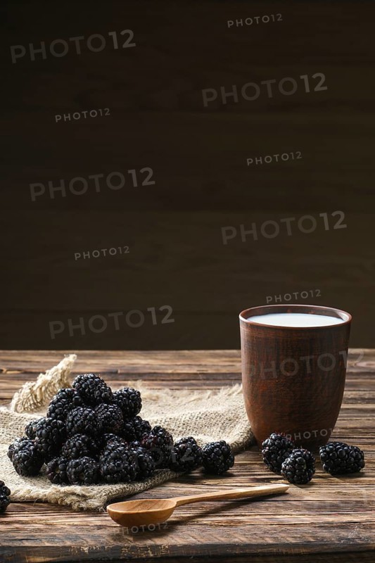 Heap of fresh dewberry on sackcloth table-napkin and clay cup with milk on wooden table