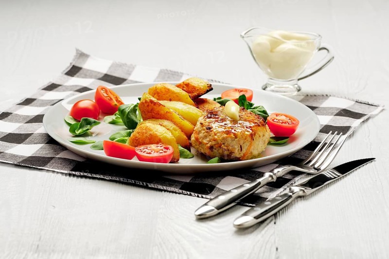 Fried chicken cutlet with potato slices served with tomato cherry and corn salad. Traditional belorussian food