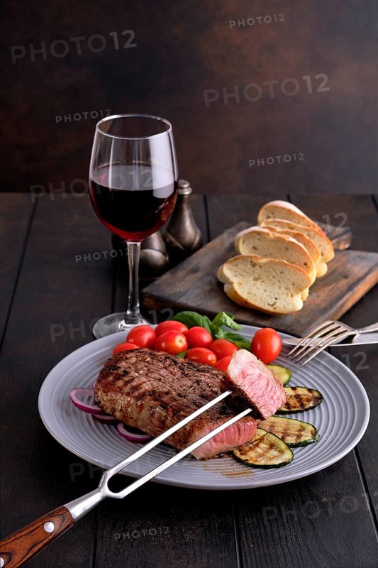 Grilled beef steak and zucchini served with fresh tomato cherry and basil and a glass of red wine