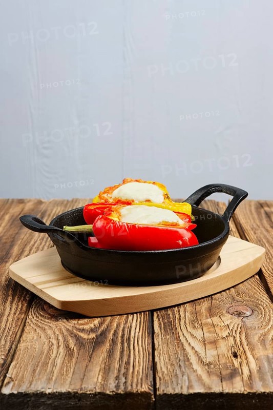 Bell pepper stuffed with meat with melted cheese mozzarella on top baked in oven in cast iron skillet. Top view. Natural wooden background