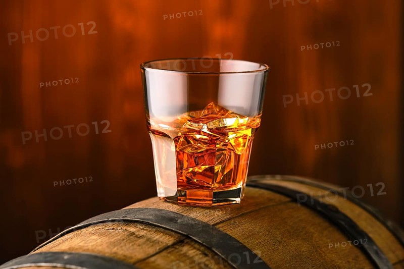 Glass of whisky with ice on the top of barrel