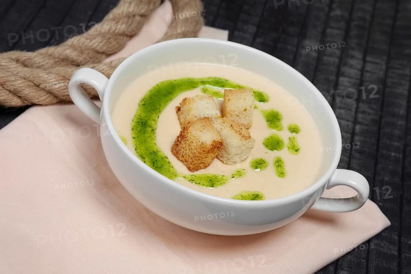 Creamy soup puree in white bowl and small pieces of fried bread toasts
