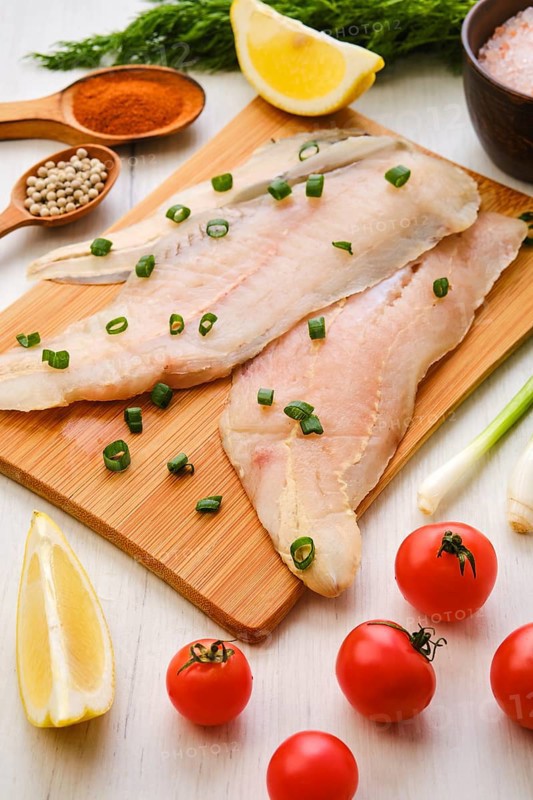 Raw fresh haddock fillet on wooden cutting board with spice and herbs