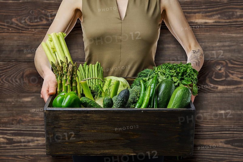 Unrecognizable wooman holds in hands wooden box with various fresh green vegetables