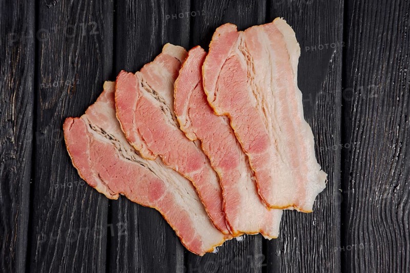 Top view of slices of fresh bacon on wooden table