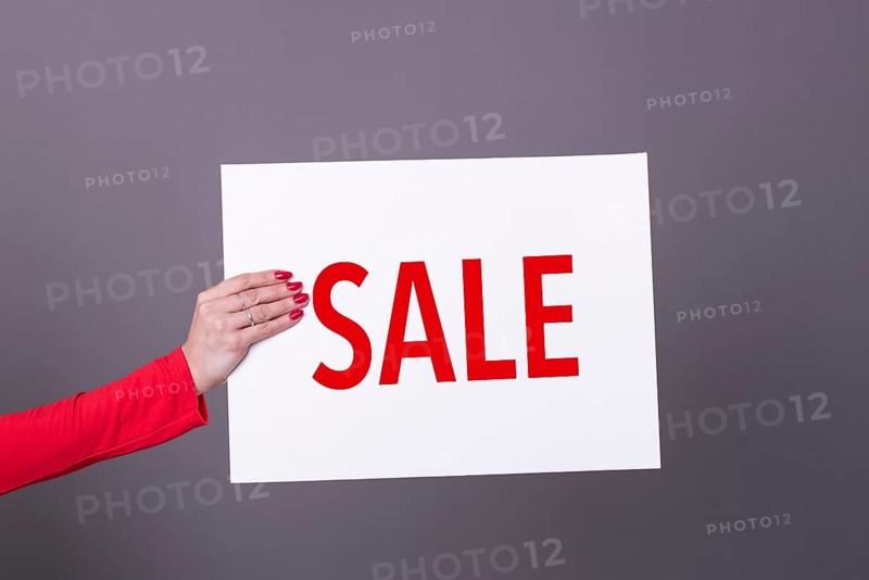 Female hand holding a Sale poster. Studio shot