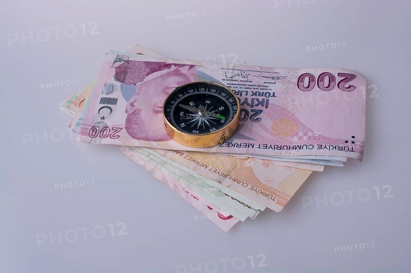 Turkish Lira banknotes by the side of a compass on white background