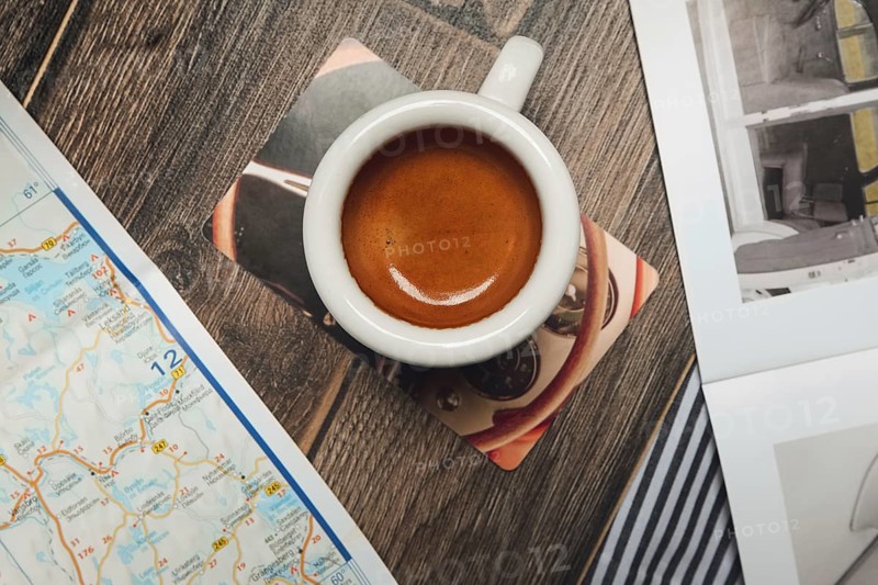 Cup of espresso near map and magazine on the table. Top point of view