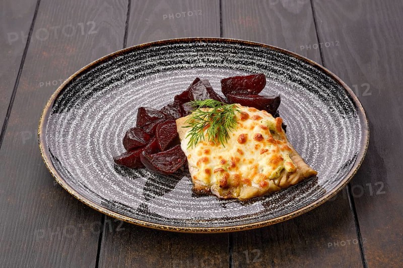 Fried cod fillet with melted cheese topping and roasted beetroot slices on dark wooden table