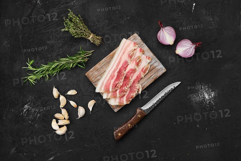 Overhead view of slices of pork bacon on wooden cutting board