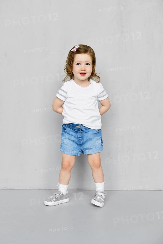 Two years old girl in white t-short and jeans shorts posing in studio