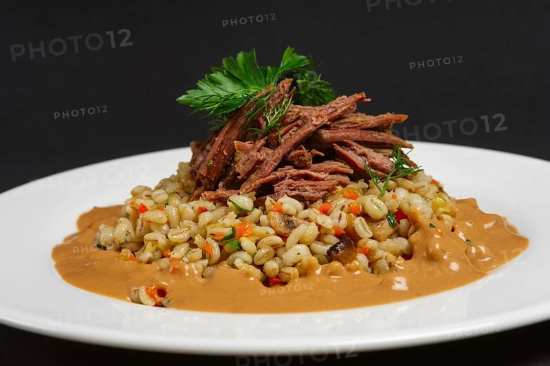Plate with boiled beef and pearl barley on black background