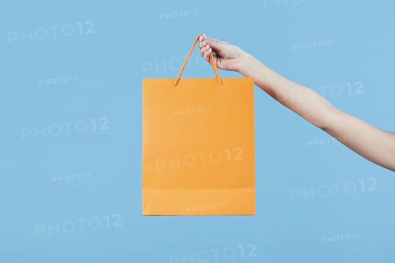 Hand holding shopping bag plain background