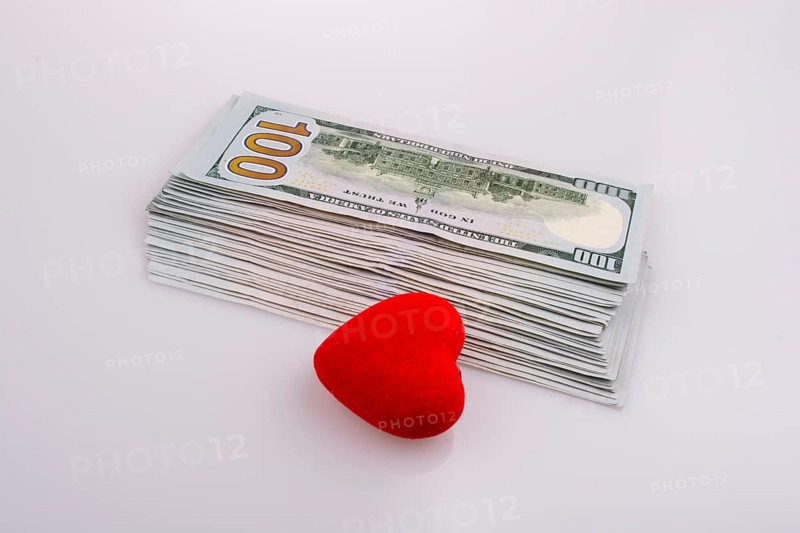 American dollar banknotes by the side of a red color heart shaped object on white background