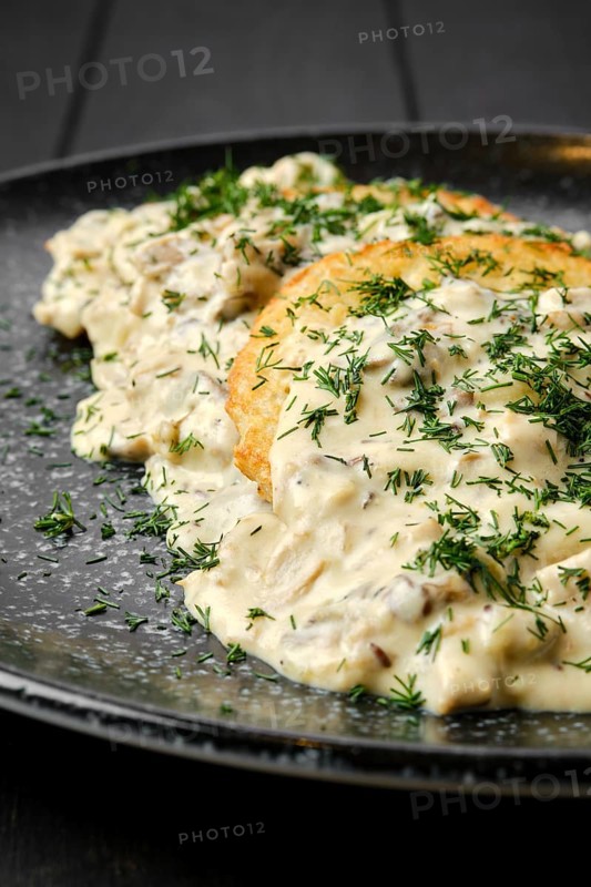 Closeup view of potato patty with fried boletus and creamy sauce on a plate