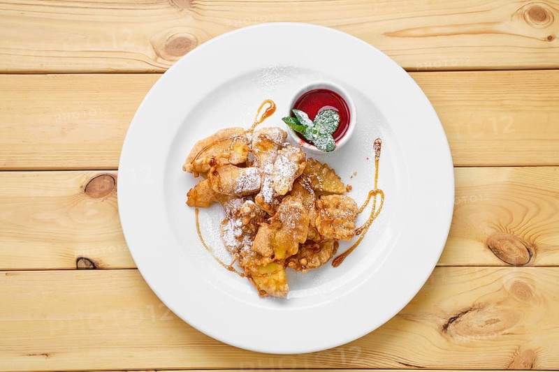 Top view of plate with deep fried fruits in breading served with caramel and strawberry jam