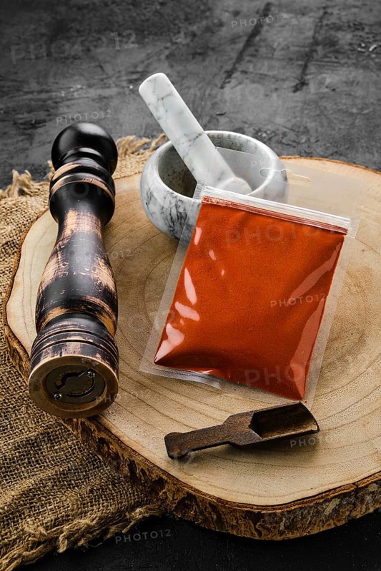 Wooden cross section with smoked paprika in plastic package and stone mortar and mill