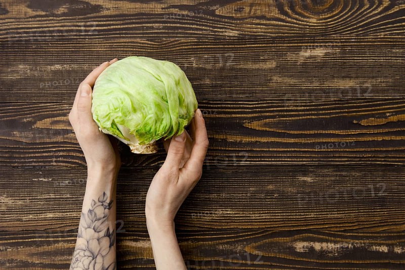 Overhead view of fresh iceberg lettuce in hands over wooden background