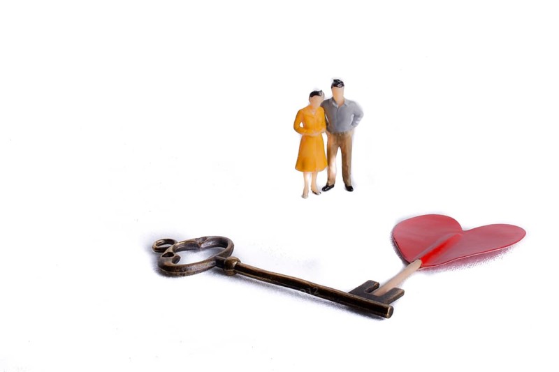 Couple standing in front of a heart shape and a key on a white background
