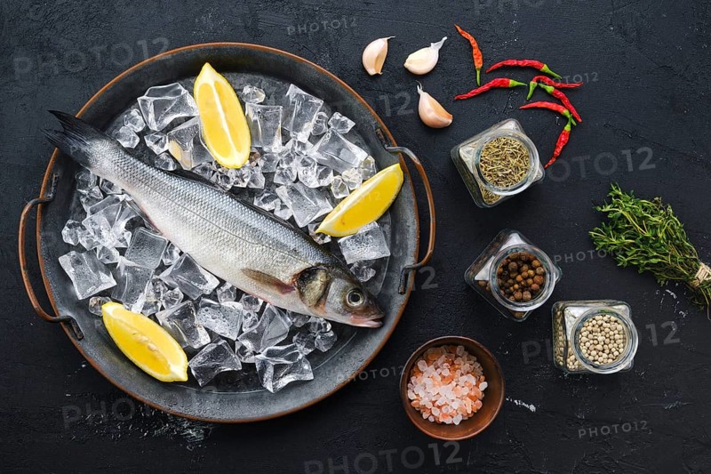 Raw seabass fish with spice and herbs on wooden background