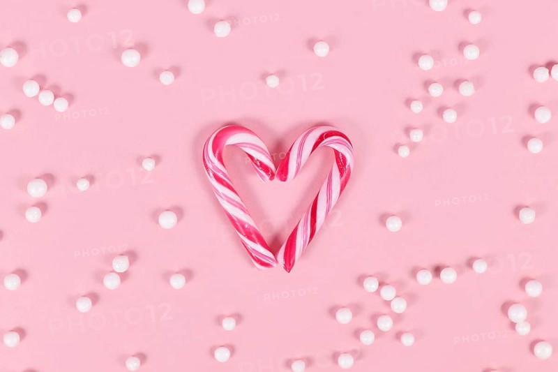 Small striped Christmas candy cane sweets forming heart on pink background