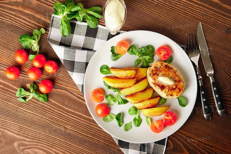 Fried chicken cutlet with potato slices served with tomato cherry and corn salad. Traditional belorussian food
