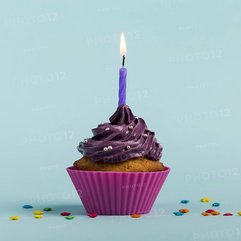 Purple burning candles decorative muffins with colorful star sprinkles against blue backdrop