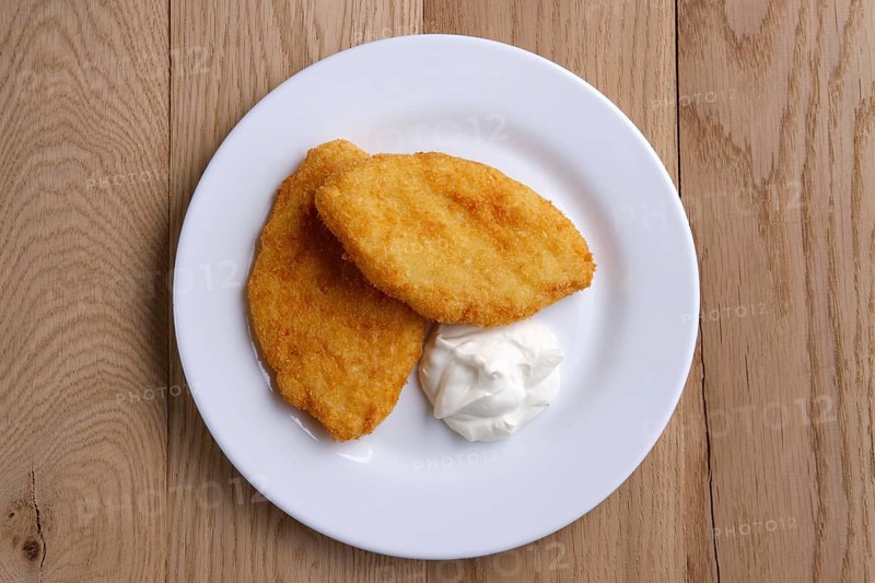 Top view of potato cutlet in breading stuffed with ham served with sour cream on wooden table