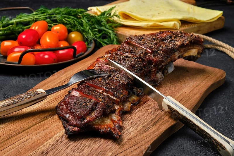 Close up view of grilled lamb breast and flap on wooden cutting board