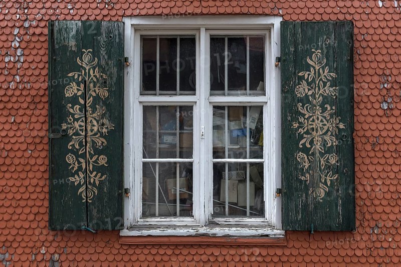Ornate shutters on a barred window on a shingle facade