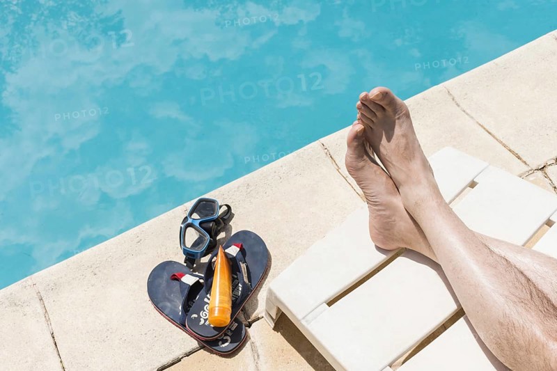 Legs near goggles with lotion flip flops near pool