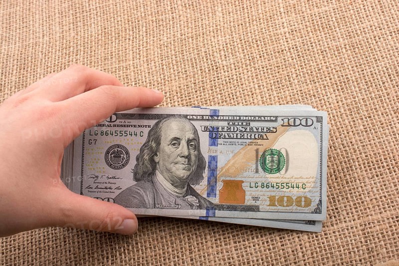 Hand holding banknote bundle of US dollar on a linen canvas background
