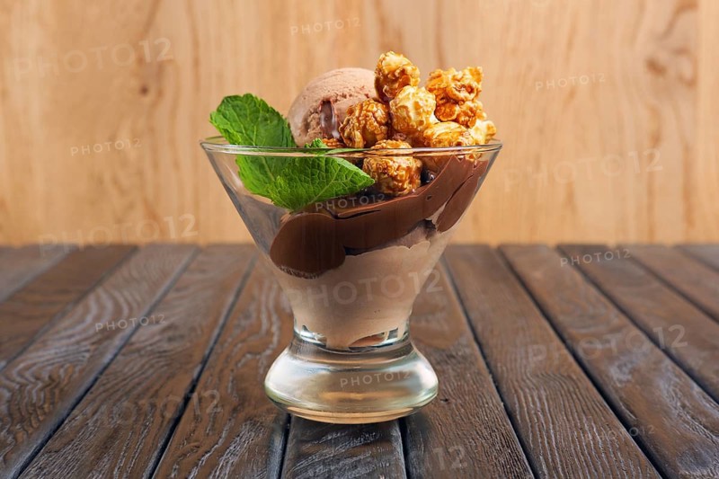 A cup of chocolate ice cream decorated with caramel popcorn and mint leaves