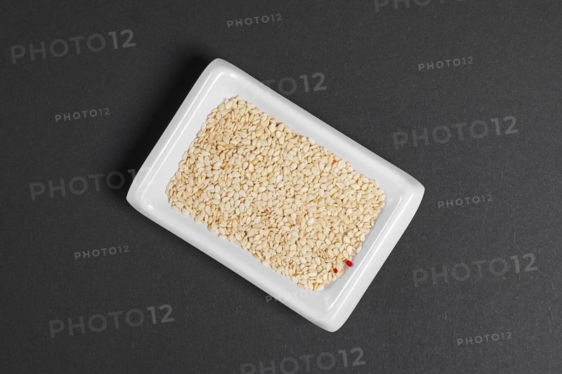 Top view of white sesame seeds in a little dish on gray paper
