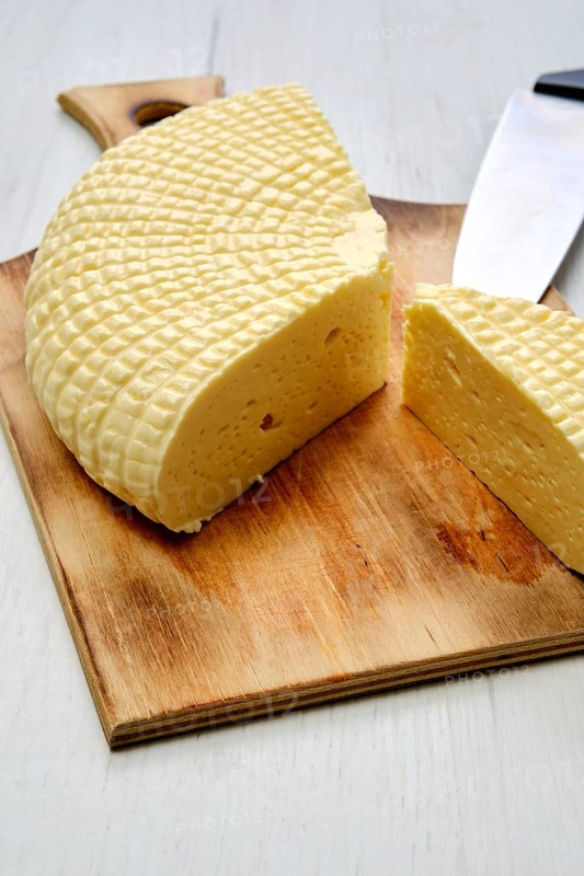 Fresh Adyghe cheese cut on slices on wooden cutting board