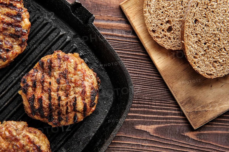 Top view of cast iron grill pan with beef cutlets and freshly baked brown bread