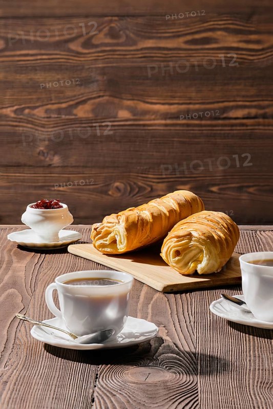 Rolled buns and coffee on wooden table in morning sunlight. Photo with shallow depth of field