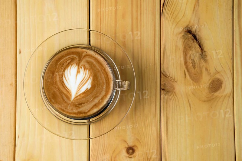 Overhead view of cappuccino in transparent glass cup on wooden table