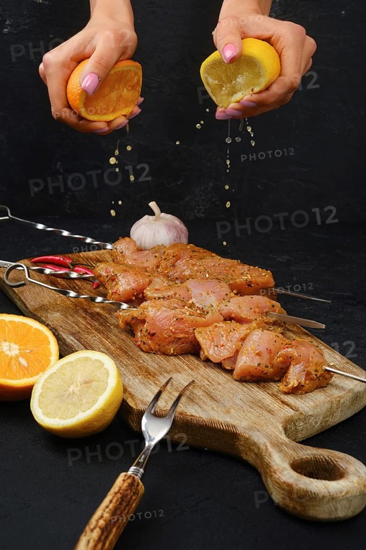 Pouring orange and lemon juice on skewers with raw turkey meat with sweet and spicy rub on dark background