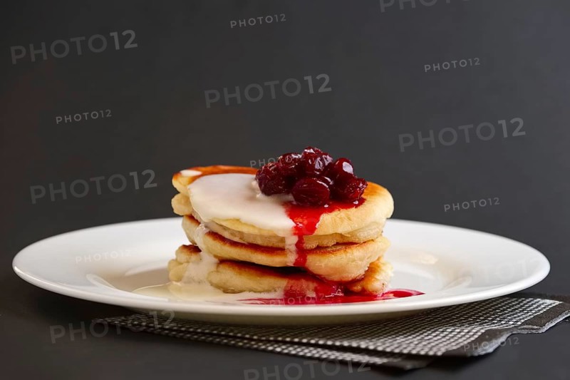 Plate with pancakes with sour cream and cherry syrup on black background