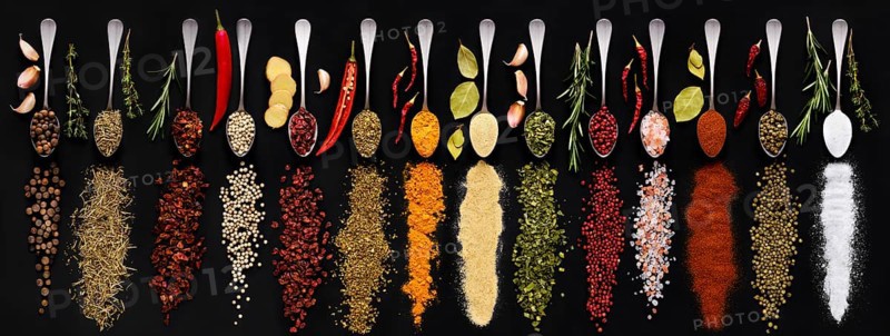 Various seasonings and herbs in spoons on dark background