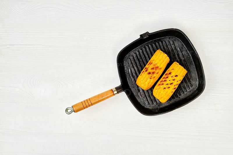 Top view at cast iron pan with grilled corn on white wooden table