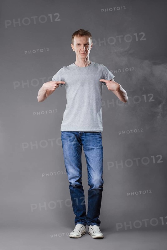 Middle age man in jeans pointing fingers to his t-shirt on gray background